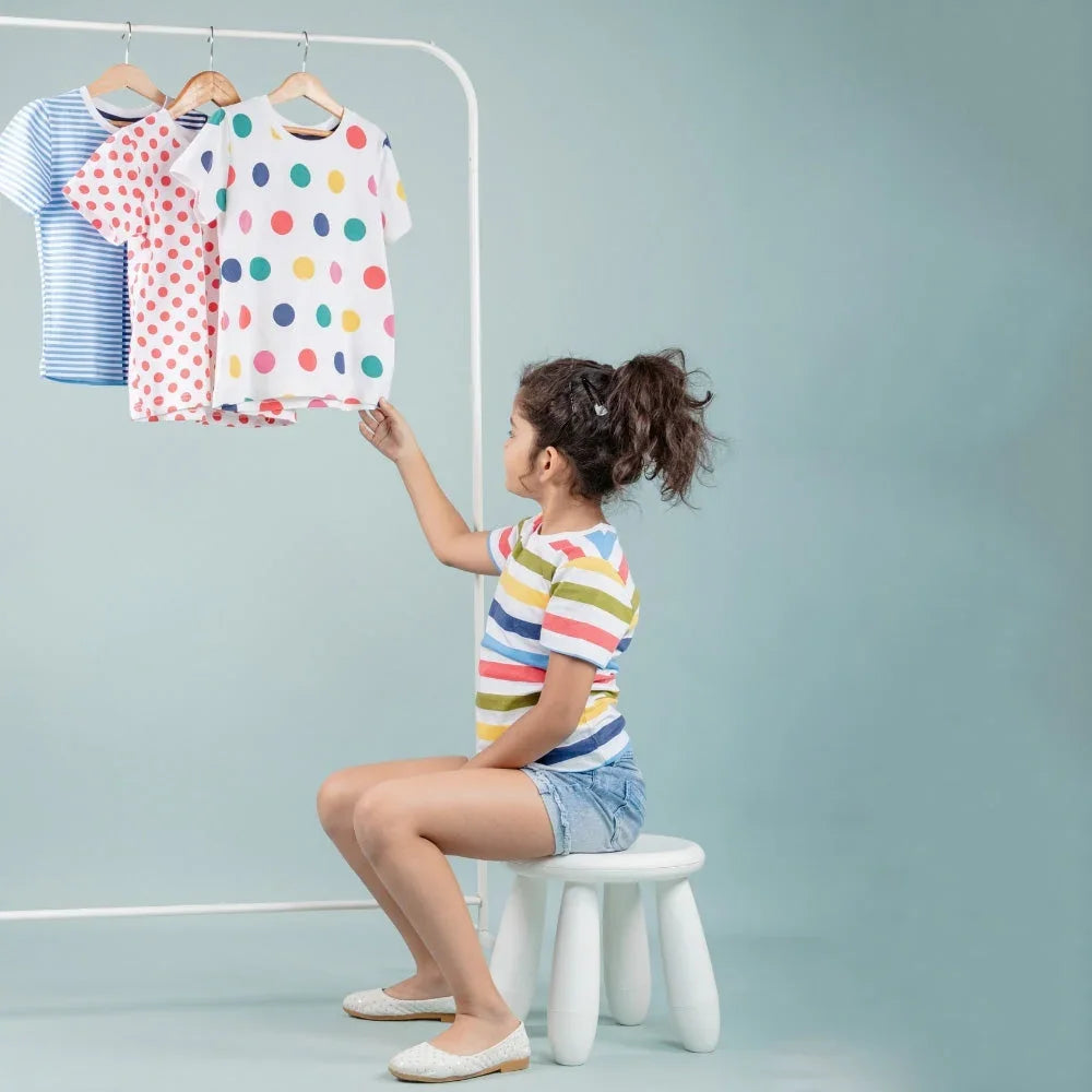 Girl in striped t-shirt and shorts choosing colorful printed t-shirts on rack, kids wear fashion