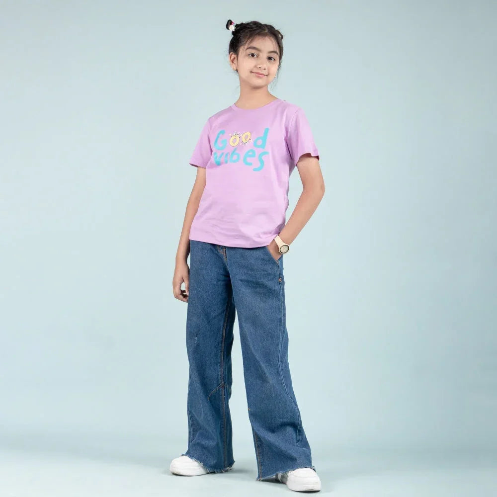 Girl wearing purple graphic t-shirt with 'Good Vibes' text and blue wide-leg jeans