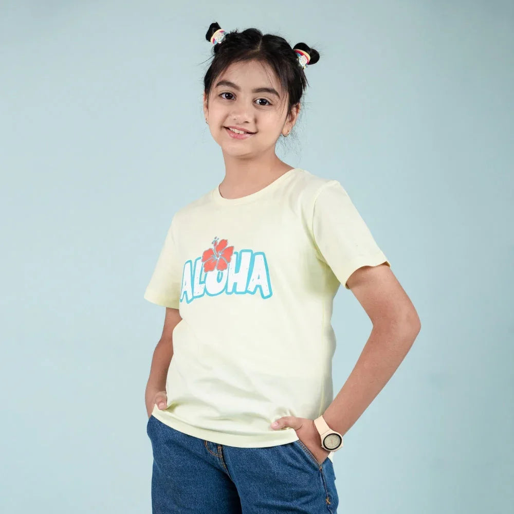Girl in yellow Aloha graphic t-shirt and blue jeans, kids fashion outfit, studio background