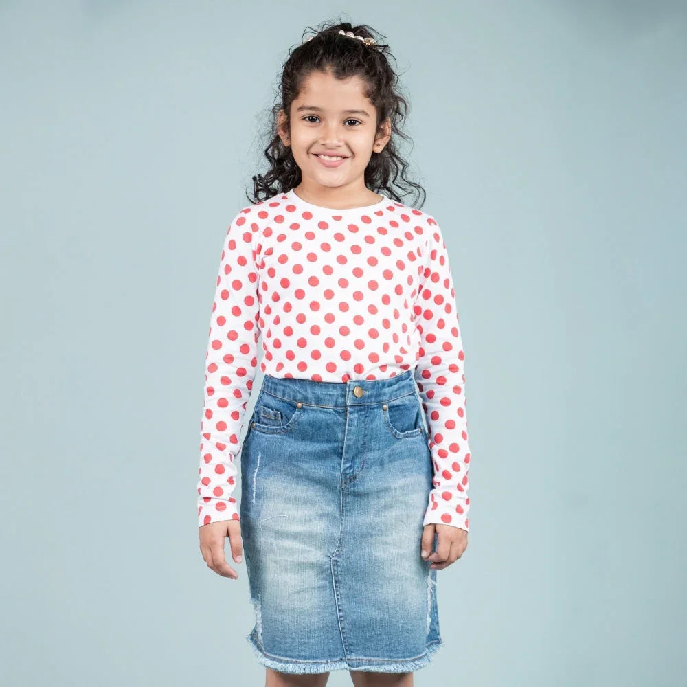 Smiling girl wearing a red polka dot long sleeve top and blue denim skirt