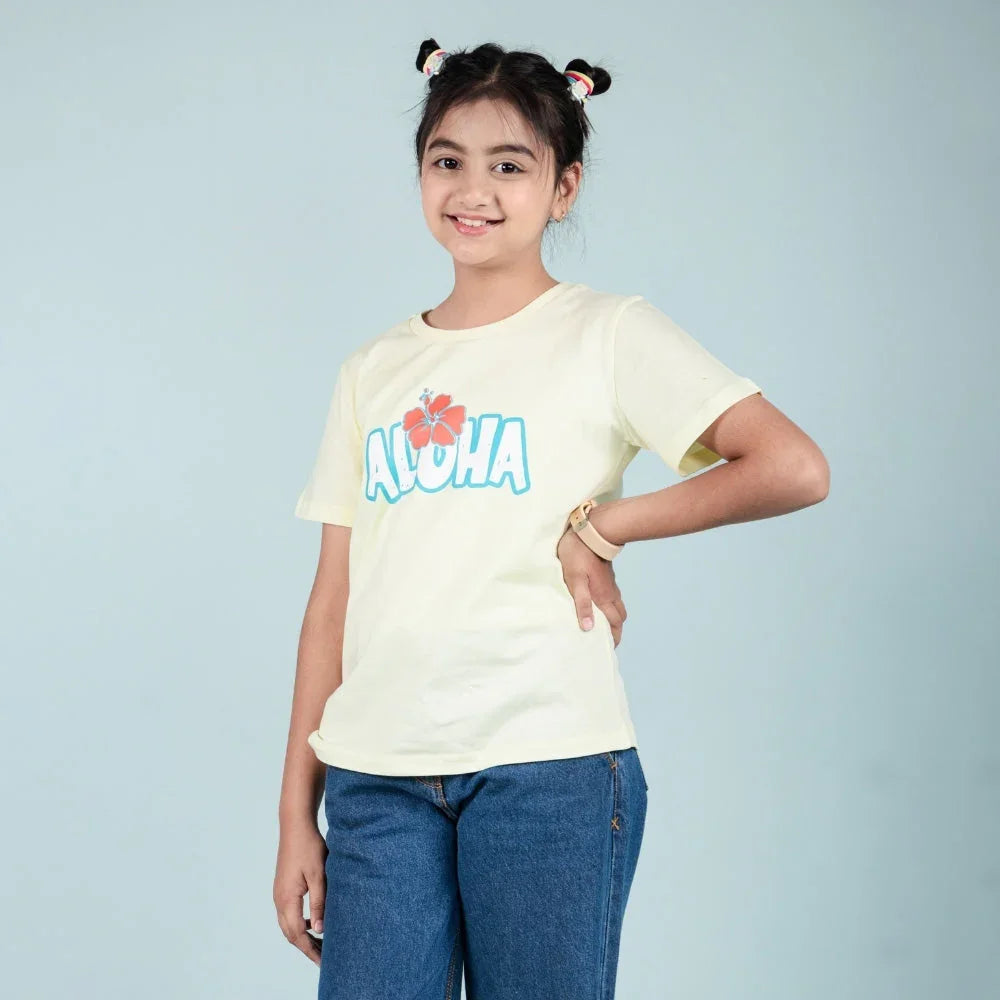 Girl wearing a yellow Aloha graphic t-shirt and blue jeans, posing against a light background