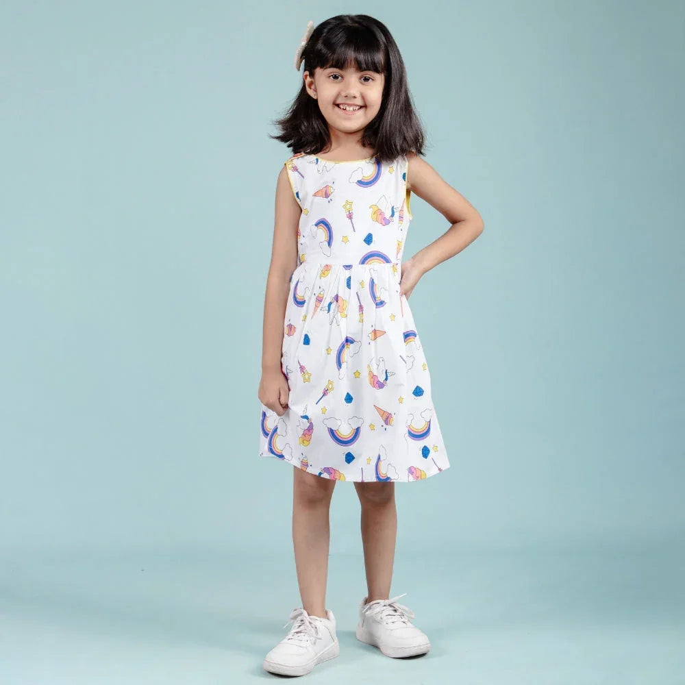 Smiling girl in sleeveless printed white dress for kids, standing against blue background