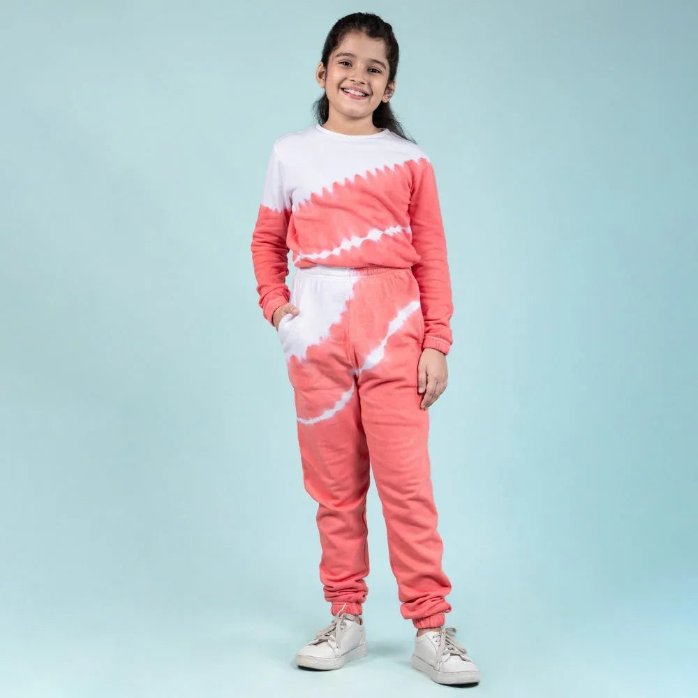 Smiling girl in coral and white tie-dye jogger set with sneakers against a blue background.