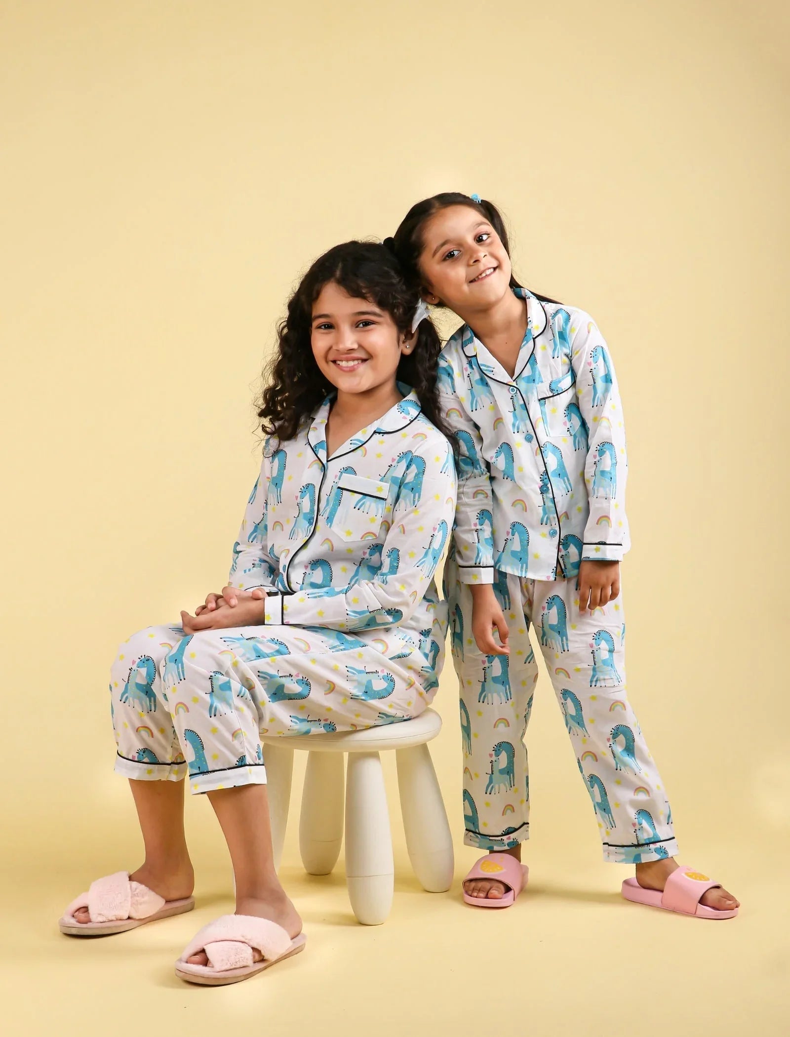 Two girls in matching dinosaur print kids sleepwear sets with slippers, beige background